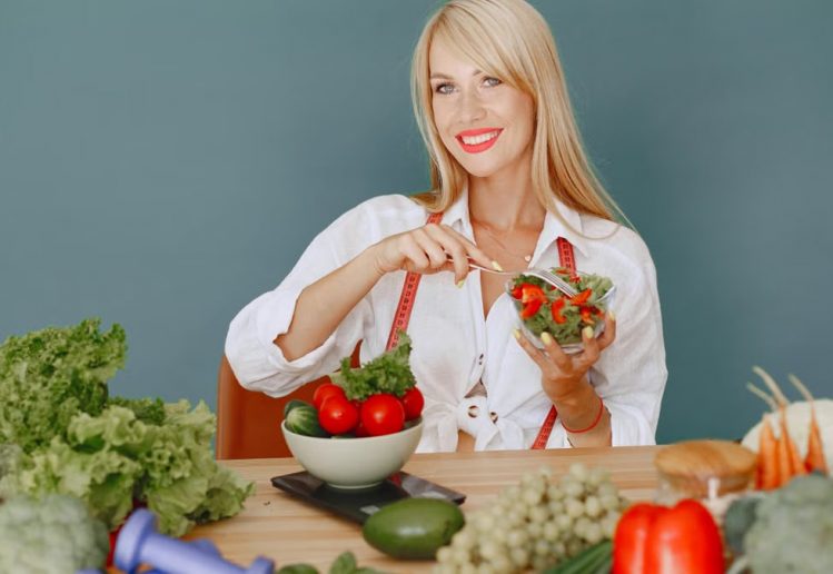 Blonde woman enjoying a fresh salad surrounded by vegetables, promoting healthy eating.