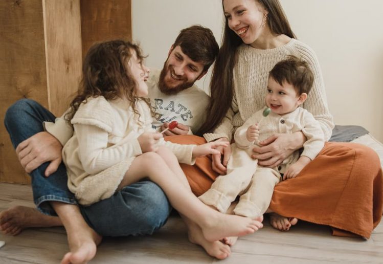 Smiling family of four sitting on the living room floor, enjoying quality time together.
