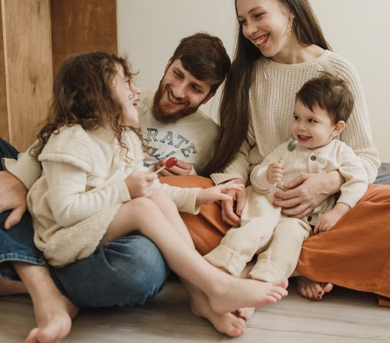 Smiling family of four sitting on the living room floor, enjoying quality time together.