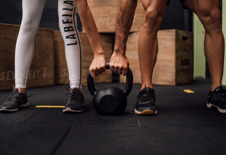 A man and woman engaging in CrossFit training with a kettlebell at an indoor gym in Brazil.